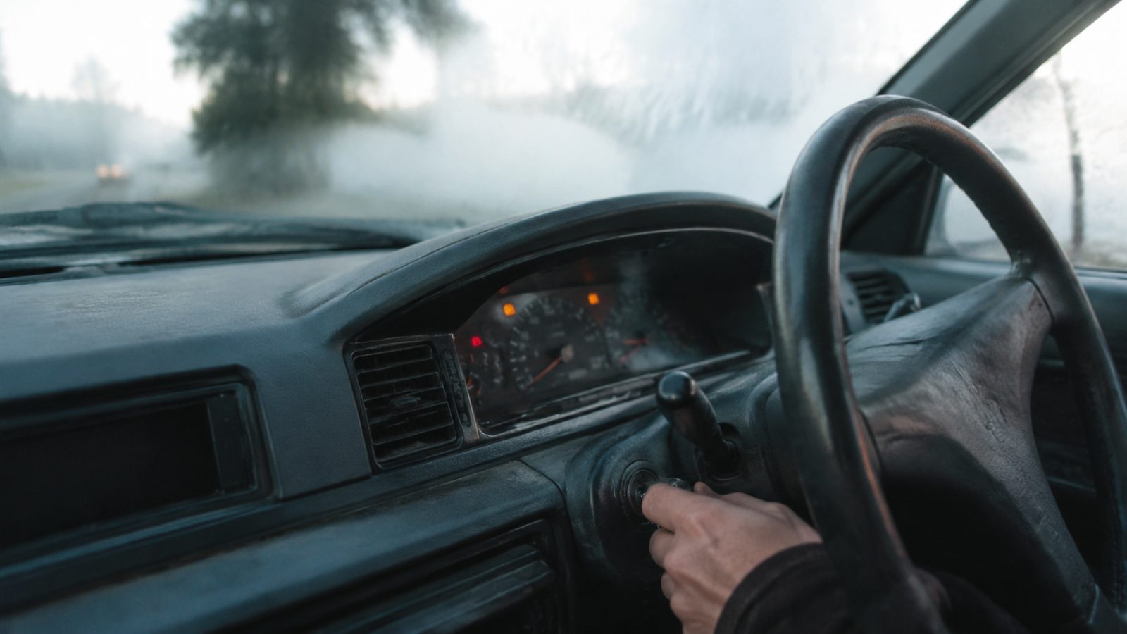 Hand turning a car key in the ignition on a cold morning with dashboard warning lights on
